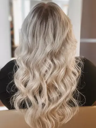 Langes, welliges blondes Haar mit dunklem Ansatz, Frisur im modernen Balayage-Stil.