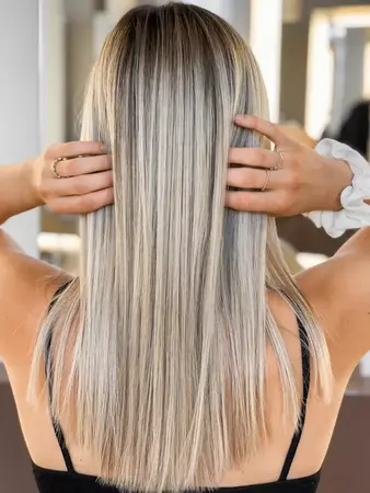 Frau mit glatten, glänzenden, blond balayage Haaren im modernen Friseursalon von hinten.
