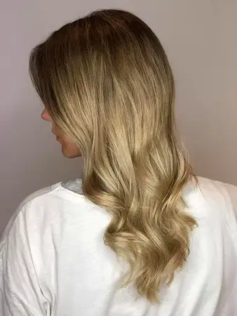 Frau mit langen, welligen, blond gesträhnten Haaren und weißem Oberteil von hinten.